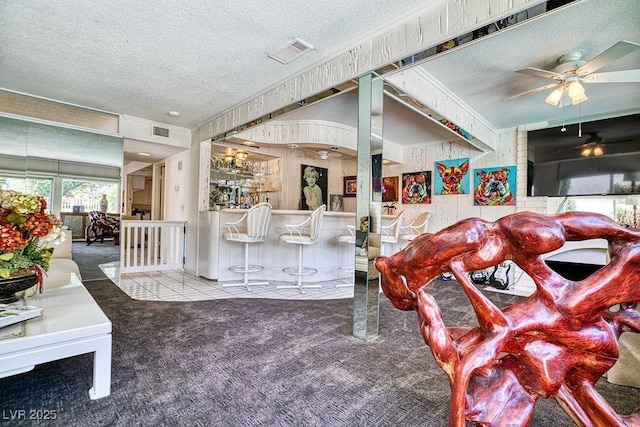 carpeted living room featuring visible vents, crown molding, a textured ceiling, and a dry bar