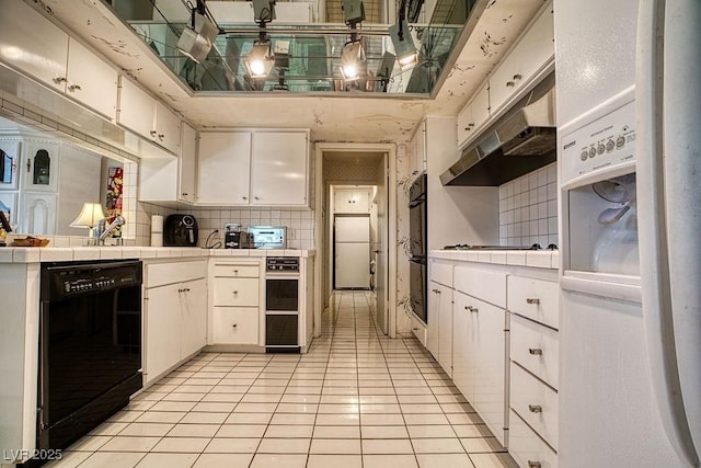 kitchen with tile countertops, under cabinet range hood, white cabinets, decorative backsplash, and black appliances