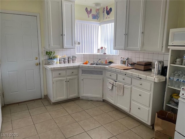 kitchen with light tile patterned floors, tasteful backsplash, tile counters, and white cabinets