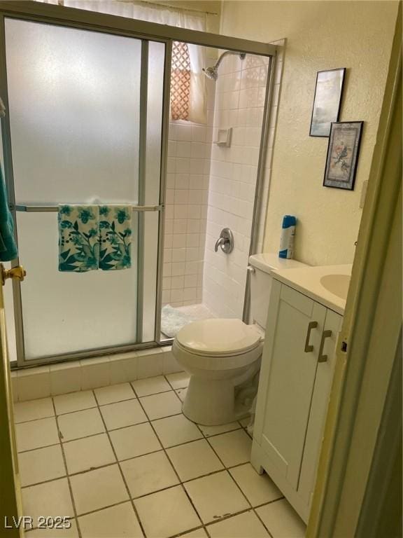 bathroom with a textured wall, toilet, a stall shower, vanity, and tile patterned floors