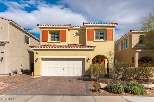 mediterranean / spanish house with a garage, fence, a tiled roof, decorative driveway, and stucco siding