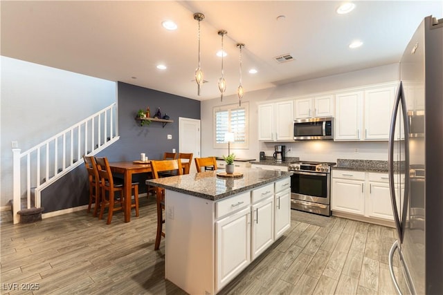 kitchen featuring light wood-style flooring, a kitchen island, visible vents, white cabinets, and appliances with stainless steel finishes