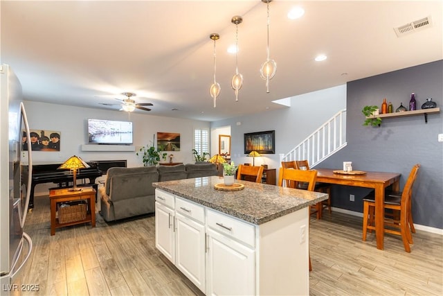 kitchen with a kitchen island, light wood-type flooring, stainless steel fridge, and visible vents