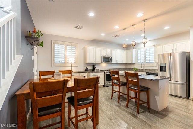 kitchen with visible vents, white cabinets, a kitchen island, appliances with stainless steel finishes, and light wood-type flooring