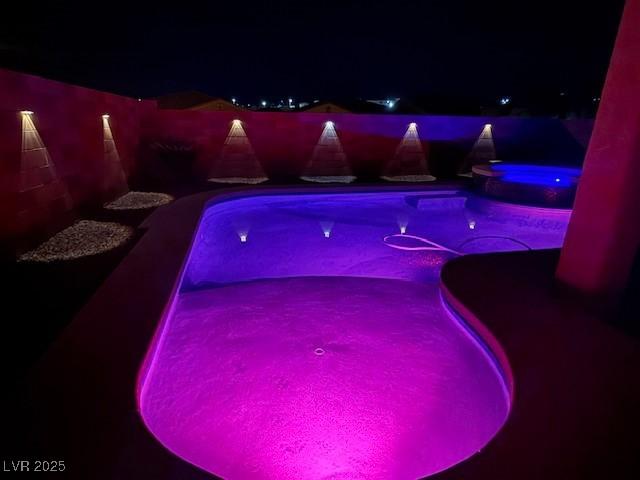 pool at twilight featuring an in ground hot tub