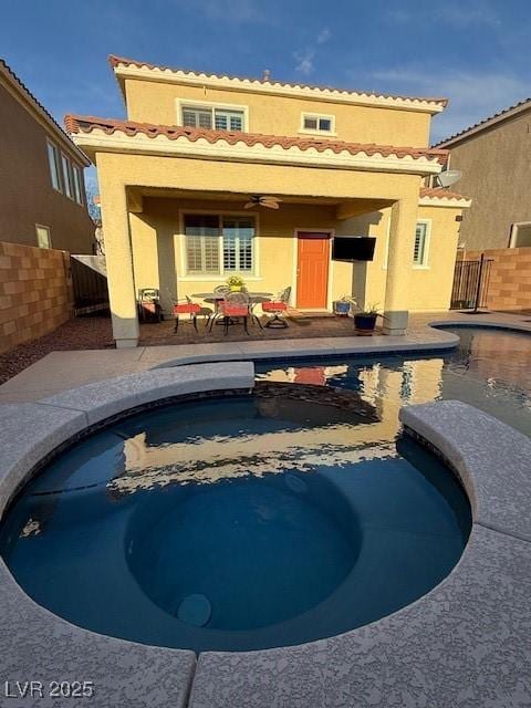 back of house featuring fence, a pool with connected hot tub, a ceiling fan, stucco siding, and a patio area