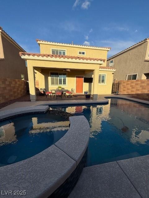 rear view of property with a pool with connected hot tub, a patio area, fence, and stucco siding