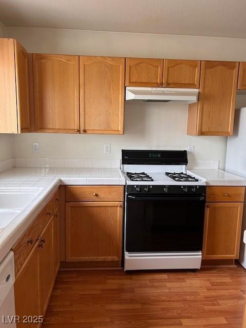 kitchen featuring tile counters, white appliances, under cabinet range hood, and wood finished floors