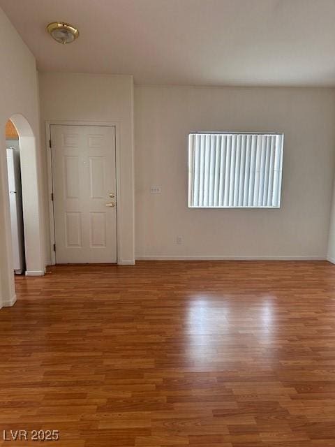 unfurnished room with arched walkways, light wood finished floors, and baseboards