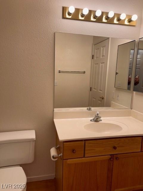 half bathroom featuring toilet, baseboards, and vanity