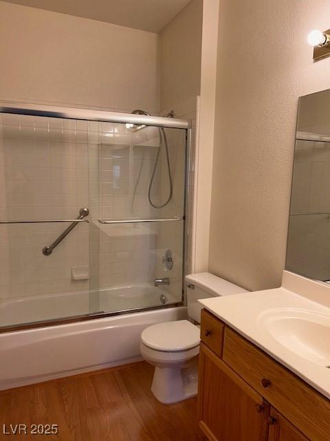 full bath with a textured wall, toilet, shower / bath combination with glass door, wood finished floors, and vanity