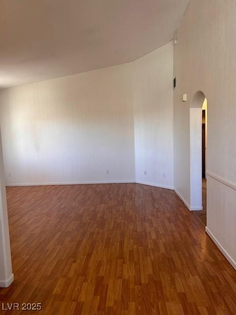 spare room featuring a towering ceiling, baseboards, arched walkways, and wood finished floors