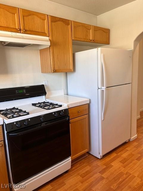 kitchen featuring light wood-style flooring, under cabinet range hood, light countertops, freestanding refrigerator, and gas range oven