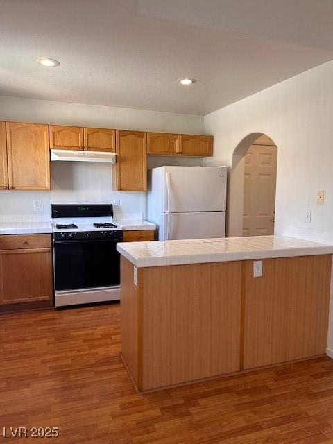 kitchen featuring tile counters, range with gas stovetop, wood finished floors, freestanding refrigerator, and under cabinet range hood