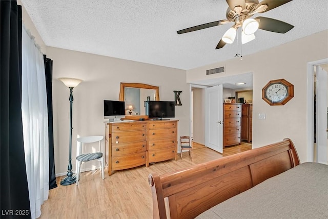 bedroom featuring light wood-type flooring, a textured ceiling, visible vents, and a ceiling fan