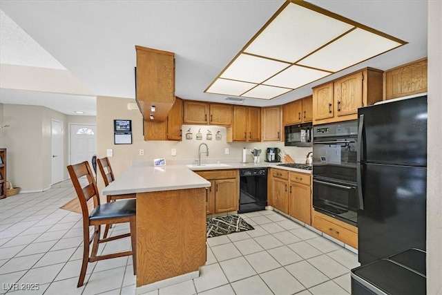 kitchen with brown cabinetry, a peninsula, black appliances, and light countertops