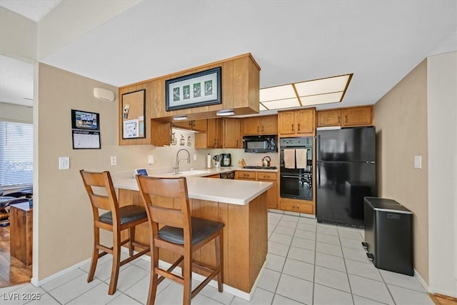 kitchen featuring a peninsula, a sink, black appliances, light countertops, and brown cabinets