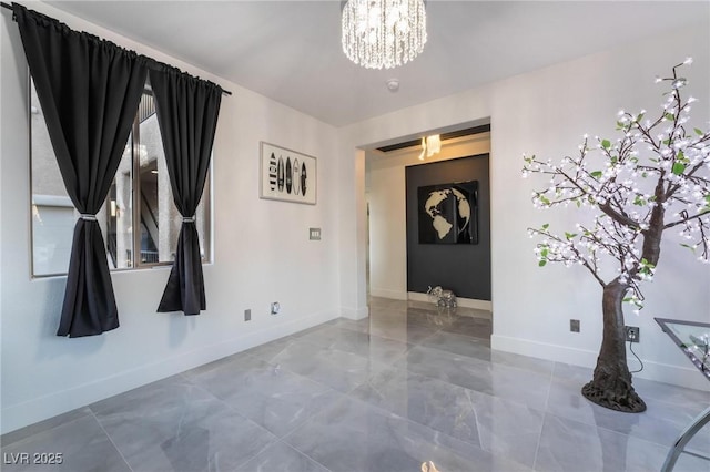 spare room featuring a chandelier and baseboards