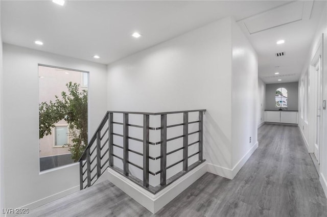 hallway featuring baseboards, visible vents, an upstairs landing, and wood finished floors