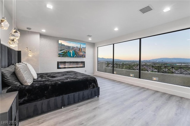 bedroom with light wood-type flooring, recessed lighting, visible vents, and a glass covered fireplace