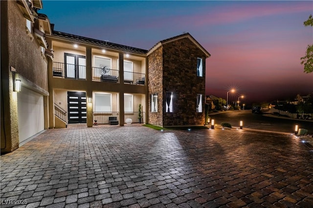 view of front of house featuring a garage, a balcony, stone siding, french doors, and stucco siding