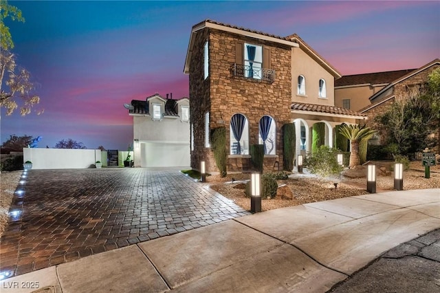 view of front of house with decorative driveway, a tile roof, stucco siding, a garage, and stone siding