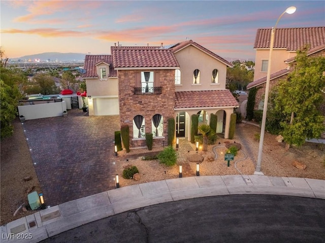 mediterranean / spanish house with stone siding, a tile roof, driveway, and stucco siding