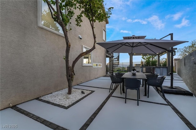 view of patio with outdoor dining space, fence, and stairs