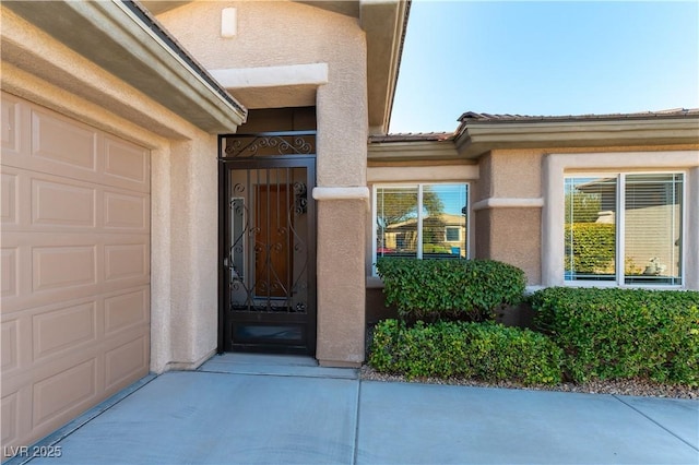 doorway to property with a garage, a tile roof, and stucco siding