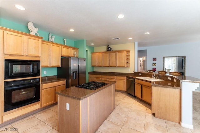 kitchen with a peninsula, a kitchen island, a sink, light brown cabinetry, and black appliances