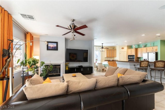 living area with light tile patterned floors, recessed lighting, visible vents, a glass covered fireplace, and ceiling fan