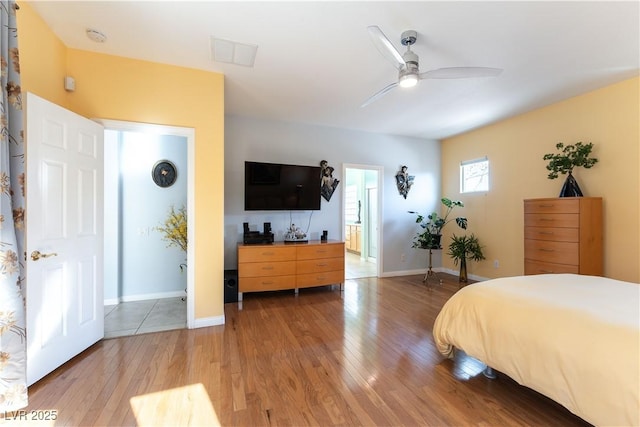 bedroom featuring visible vents, ensuite bathroom, light wood-style floors, ceiling fan, and baseboards