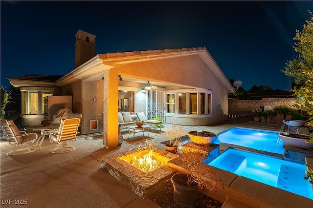 pool at night with a ceiling fan, a patio area, fence, and a fire pit