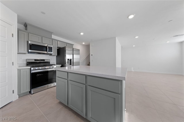 kitchen featuring light tile patterned floors, appliances with stainless steel finishes, a center island, gray cabinetry, and recessed lighting