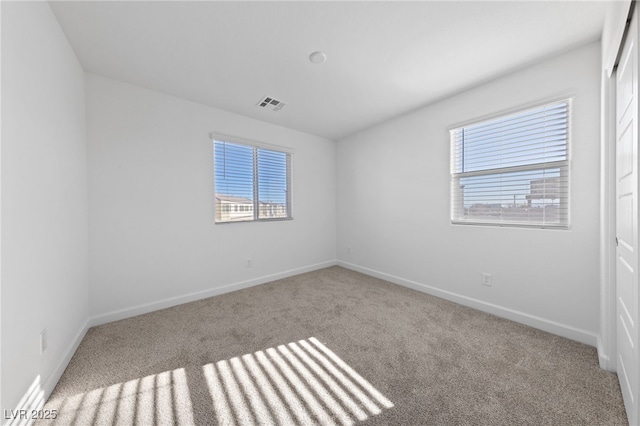 carpeted empty room with a healthy amount of sunlight, visible vents, and baseboards