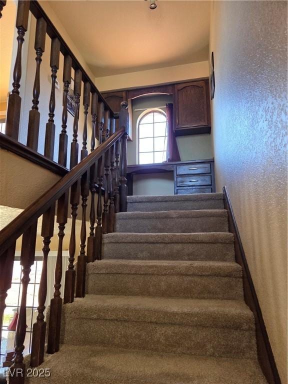 staircase featuring a textured wall and baseboards