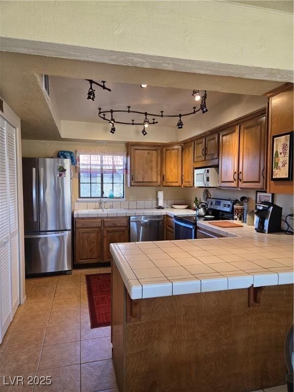 kitchen with appliances with stainless steel finishes, brown cabinets, and tile counters