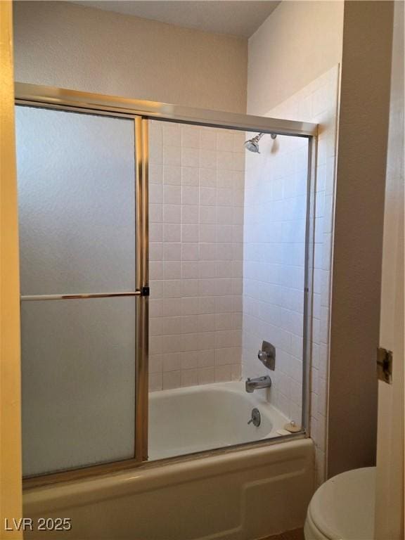 bathroom featuring toilet and bath / shower combo with glass door