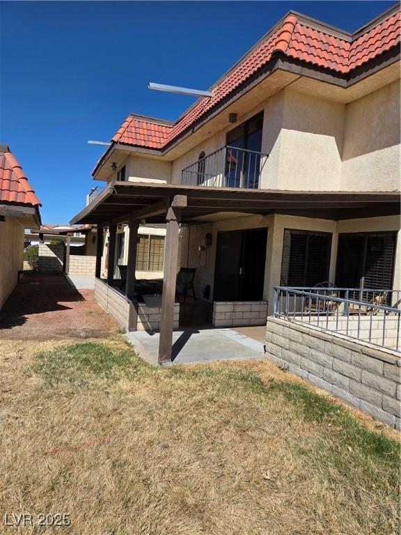 rear view of house with a tile roof, stucco siding, a patio area, fence, and a balcony