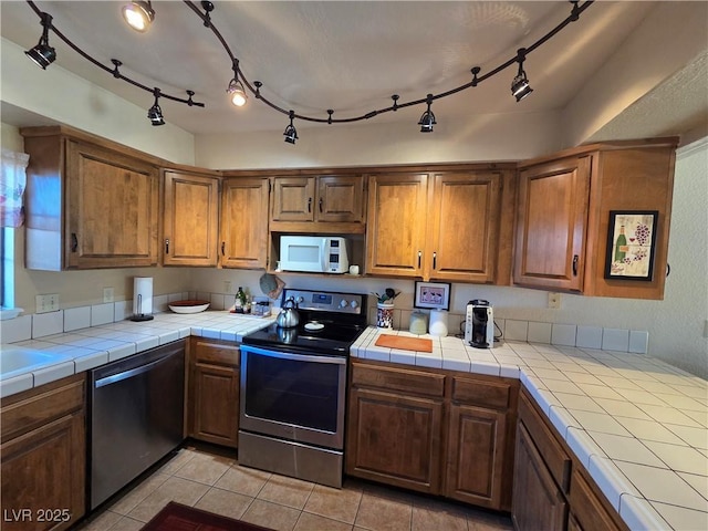 kitchen featuring tile countertops, stainless steel appliances, light tile patterned flooring, and brown cabinets