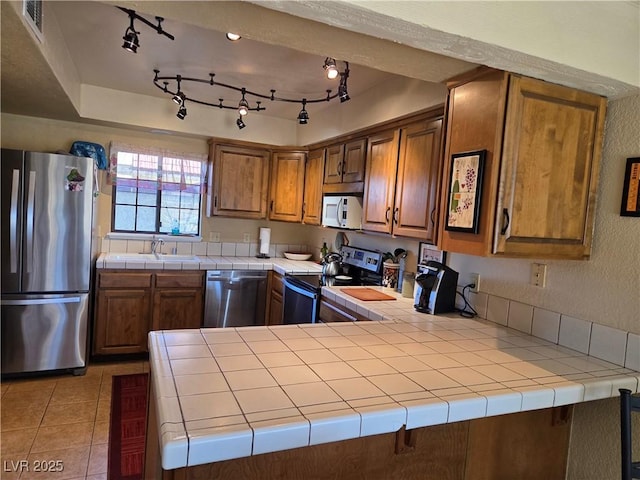 kitchen featuring appliances with stainless steel finishes, brown cabinetry, a sink, and tile counters