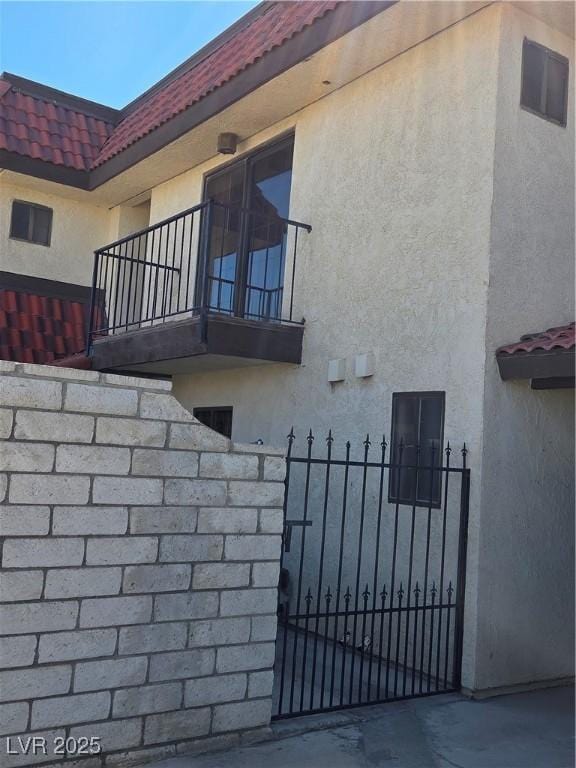 view of side of property with a balcony, a tile roof, a gate, fence, and stucco siding