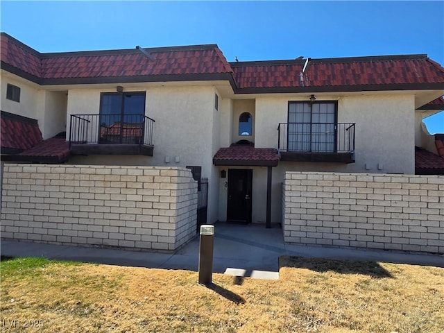 multi unit property featuring mansard roof, a tile roof, a balcony, and stucco siding