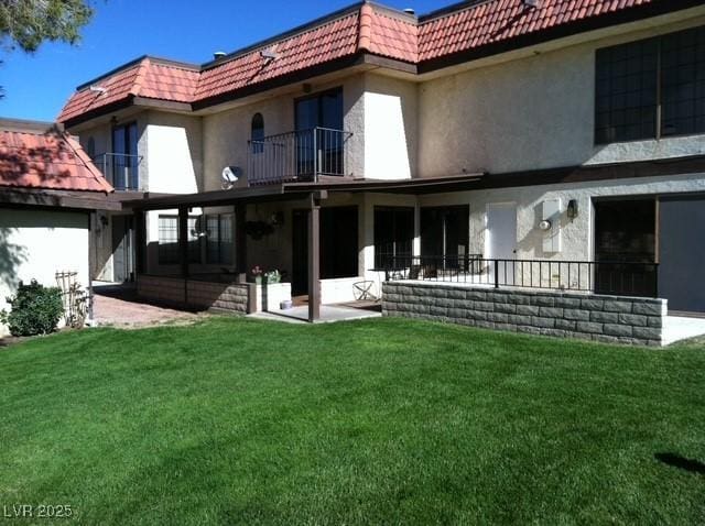 rear view of house with a tiled roof, a lawn, a balcony, and mansard roof