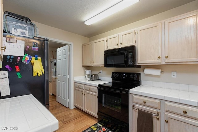 kitchen featuring light wood-type flooring, tile countertops, and black appliances