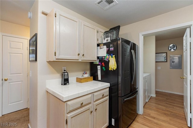 kitchen with washer and clothes dryer, light wood finished floors, visible vents, freestanding refrigerator, and electric panel