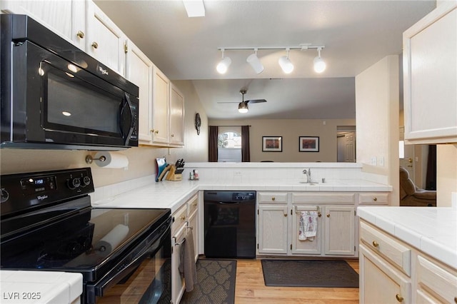 kitchen featuring light wood finished floors, tile counters, a ceiling fan, a peninsula, and black appliances