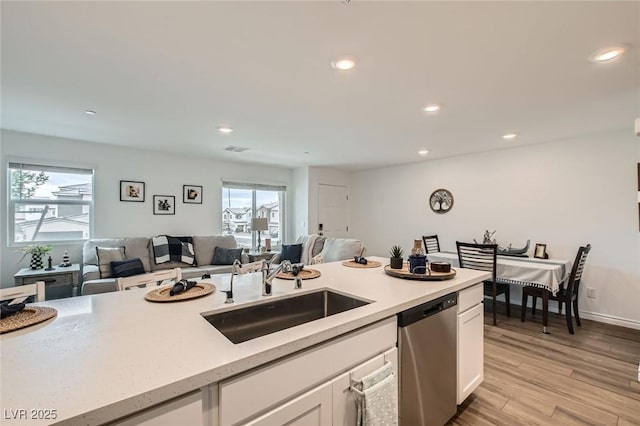 kitchen featuring dishwasher, open floor plan, light countertops, white cabinetry, and a sink