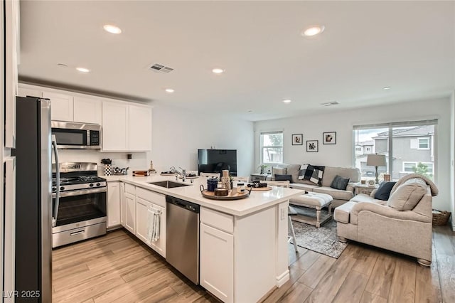 kitchen with visible vents, open floor plan, a peninsula, stainless steel appliances, and a sink