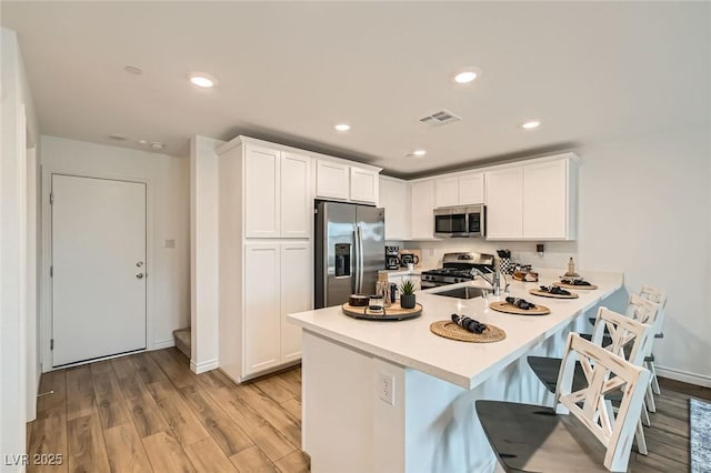 kitchen featuring a peninsula, visible vents, light countertops, appliances with stainless steel finishes, and light wood finished floors